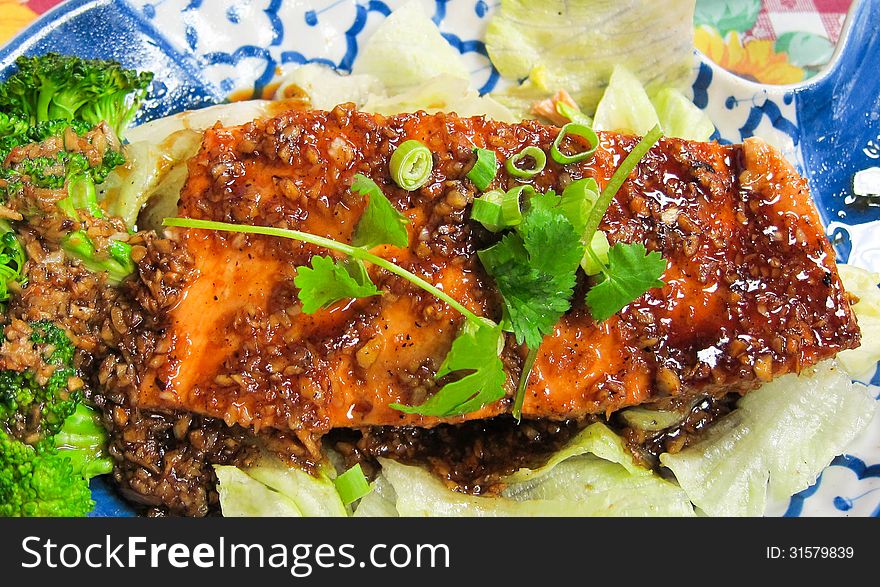 A baked salmon fillet with garlic sauce settled on a bed of lettuce. Thai cuisine.