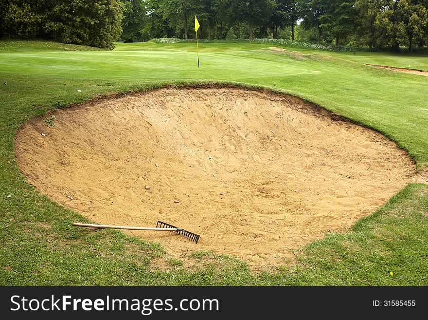 Rake lying in bunker on edge of green on gold course. Rake lying in bunker on edge of green on gold course