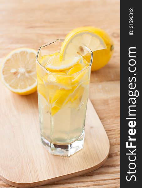 Lemon drink in a glass and lemons on a wooden surface