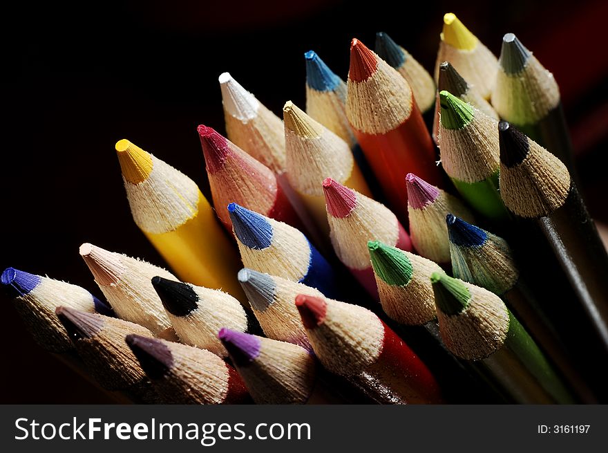 Colorful assortment of drawing pencils bunched together against a dark background. Colorful assortment of drawing pencils bunched together against a dark background