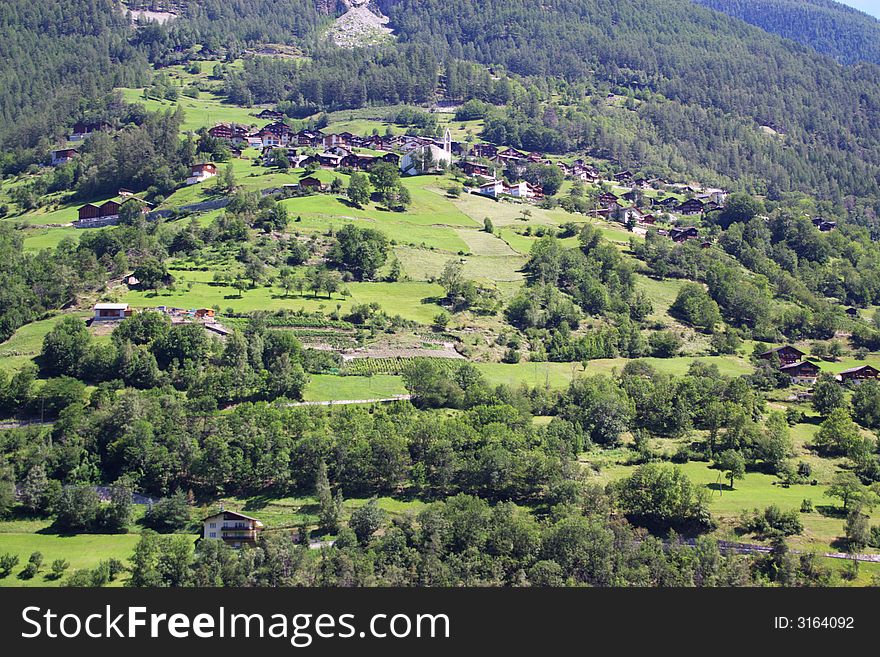 Countryside authentic alpine mountain landscape with green slopes, pastures, trees and village roofs in front. alps, Switzerland; Europe. Countryside authentic alpine mountain landscape with green slopes, pastures, trees and village roofs in front. alps, Switzerland; Europe