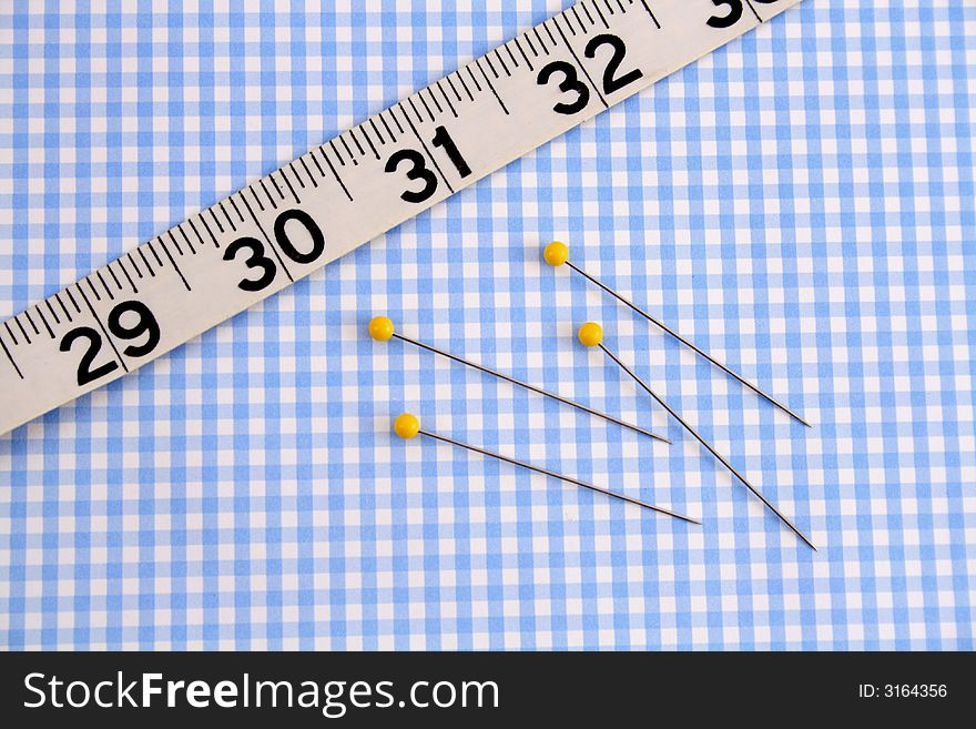 Measuring tape and quilting pins on a gingham background. Measuring tape and quilting pins on a gingham background