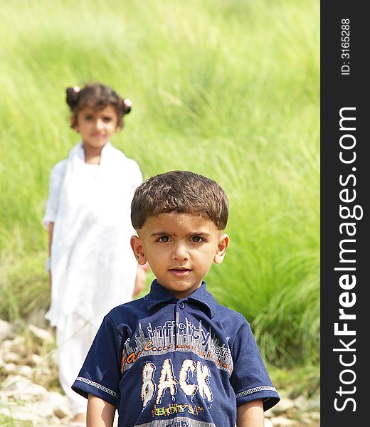 Young Asian boy looking directly at camera; sister is looking on in the background, slightly blurred. Young Asian boy looking directly at camera; sister is looking on in the background, slightly blurred.