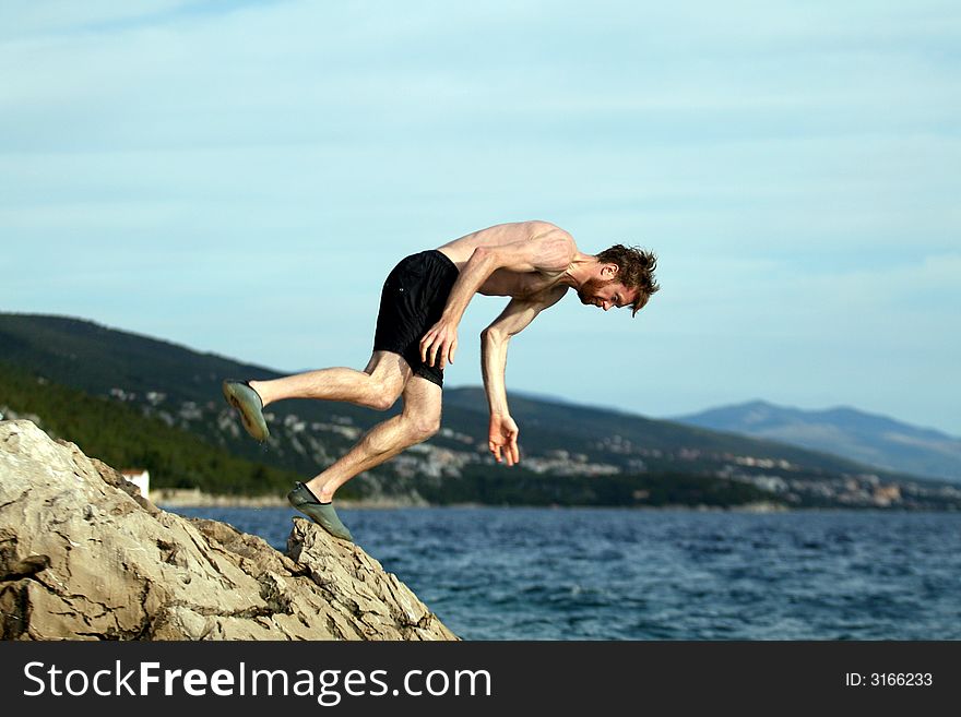 A young man summersaults from a cliff into the sea!. A young man summersaults from a cliff into the sea!