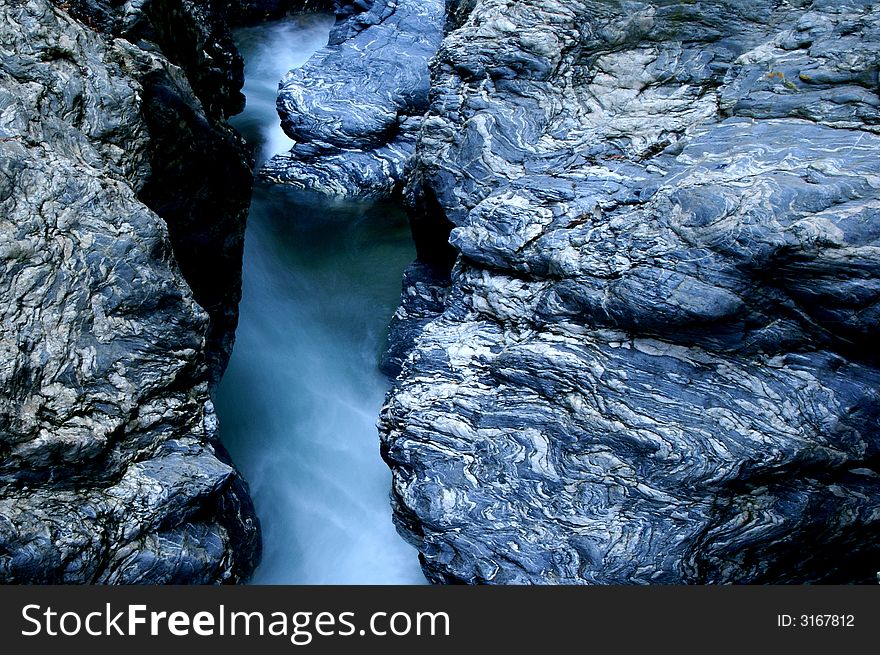 Motion-blurred water stream between massive rocks with interesting structure.