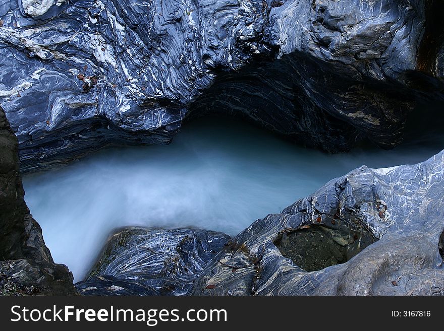 Motion-blurred water stream between massive rocks with interesting structure.