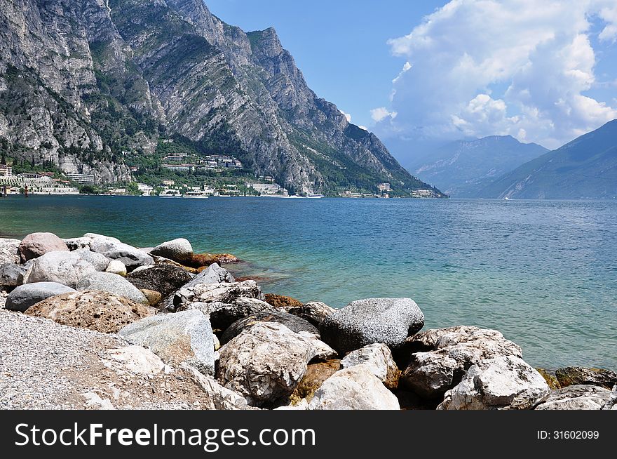 Image shows Limone on the left, Lake Garda in the middle, some mountains on both sides and stony beach in the front. Image shows Limone on the left, Lake Garda in the middle, some mountains on both sides and stony beach in the front.