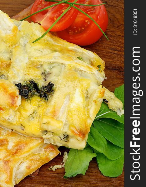 Slices of Cheese and Greens Pie Garnished with Tomatoes, Spring Onion and Basil on Wooden Plate closeup