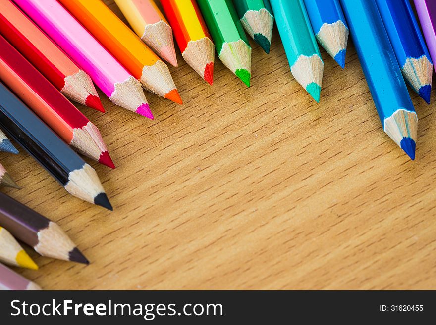 Line of colored pencils on wooden background