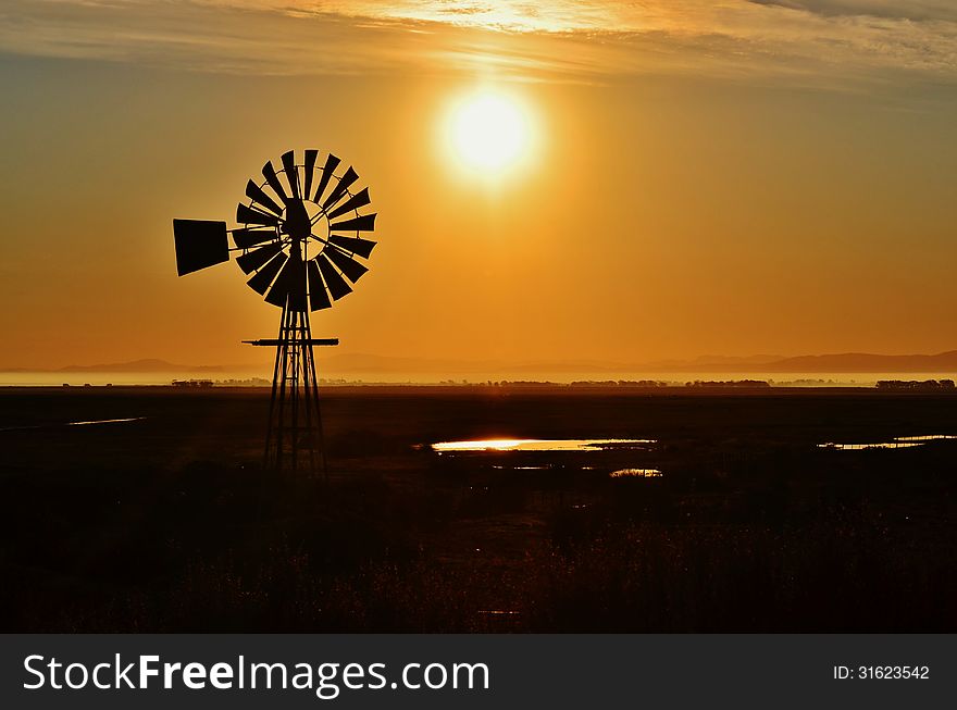 Landscape with windmill waterpump at sunrise