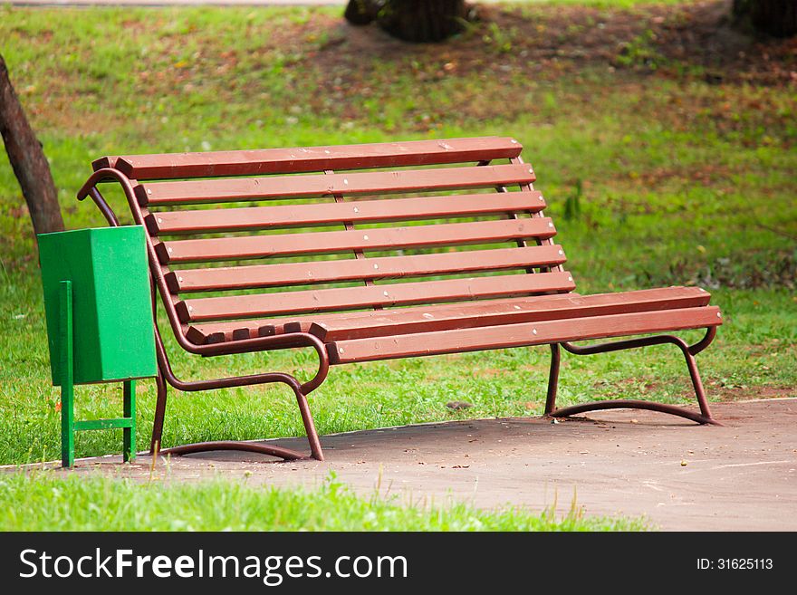 Old brown wooden bench in the park on a background of green grass in the shadow. Old brown wooden bench in the park on a background of green grass in the shadow