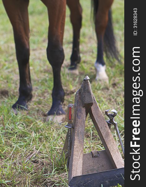 A farrier's hoof stand, tools attached, with a horse standing in the background. A farrier's hoof stand, tools attached, with a horse standing in the background.