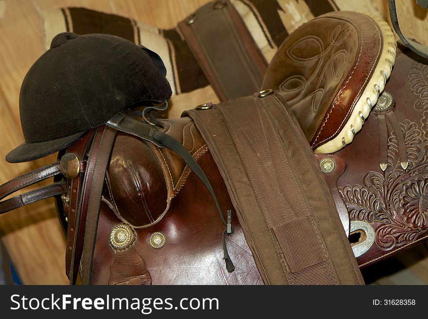 A Black, English helmet resting on the horn of a brown, leather, tooled, western saddle. A Black, English helmet resting on the horn of a brown, leather, tooled, western saddle.