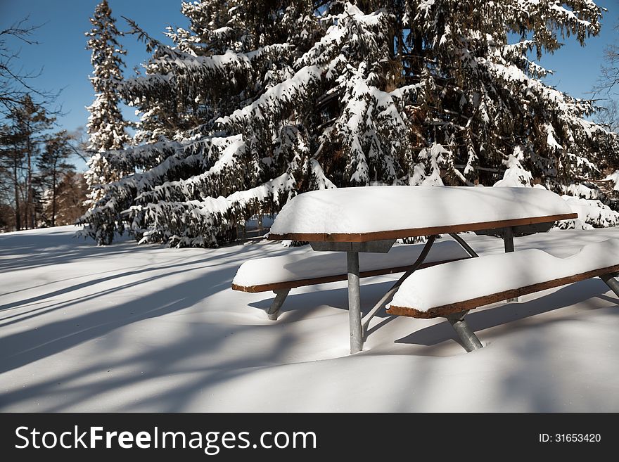 View of winter park and picnic table covered by thick layer of snow. View of winter park and picnic table covered by thick layer of snow