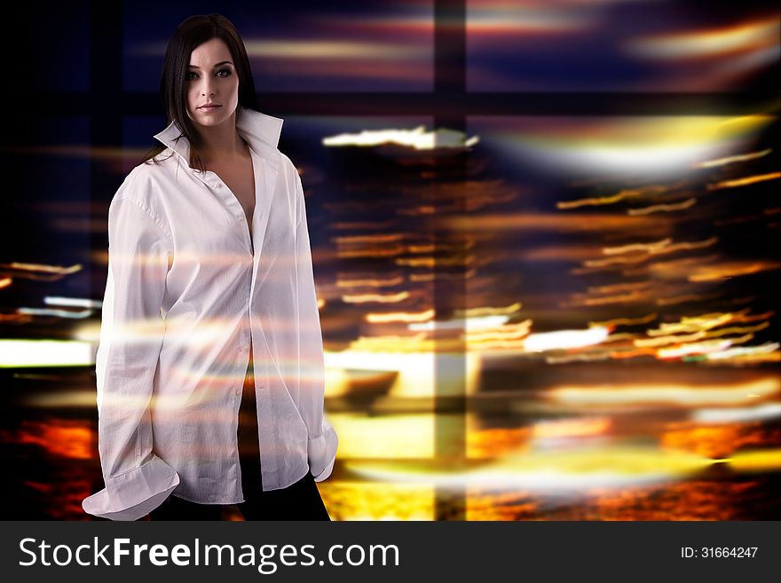 Attractive brunette woman wearing big size white shirt is standing over colorful, unfocused moving lights background. Attractive brunette woman wearing big size white shirt is standing over colorful, unfocused moving lights background.
