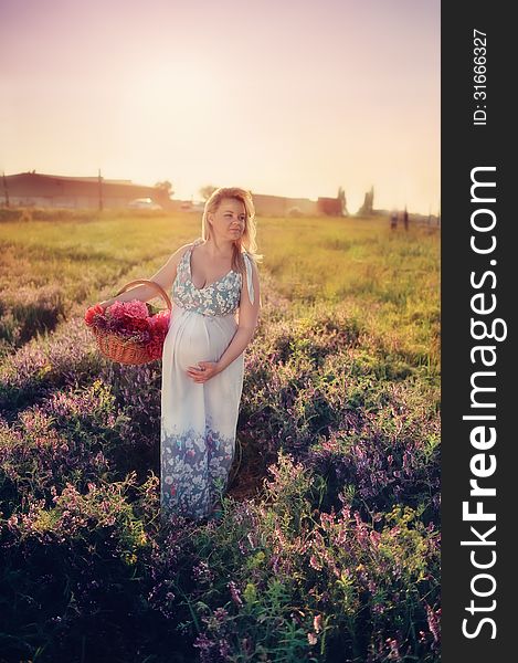 At sunset walks on the field a pregnant woman with a basket of flowers. At sunset walks on the field a pregnant woman with a basket of flowers