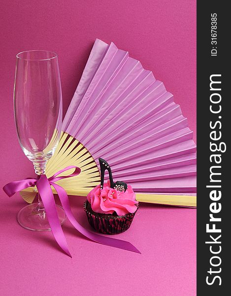 Pink party decorations with fan, champagne glass and high heel shoe cupcake - vertical.