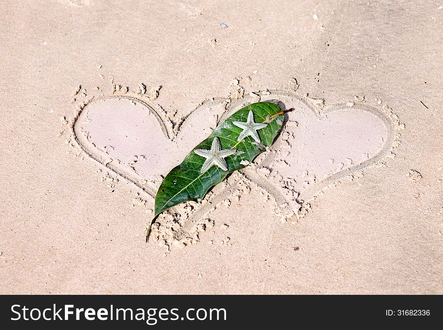 Still life with two drawn hearts and starfishes on wet sand