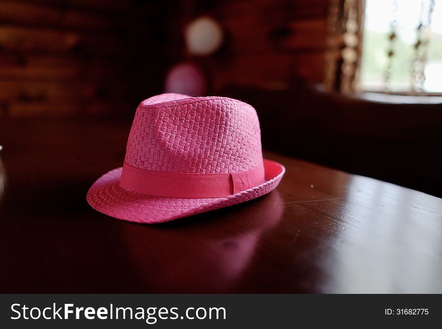 On a brown wooden table is a beautiful stylish pink hat