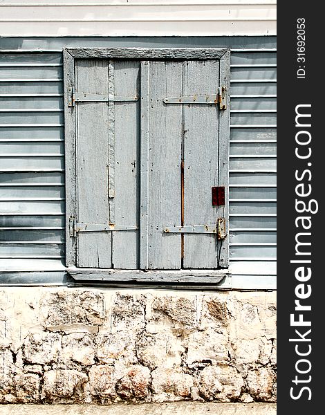 Image of an old window with wooden shutters set in a wall of stone and corrugated iron sheets. Image of an old window with wooden shutters set in a wall of stone and corrugated iron sheets