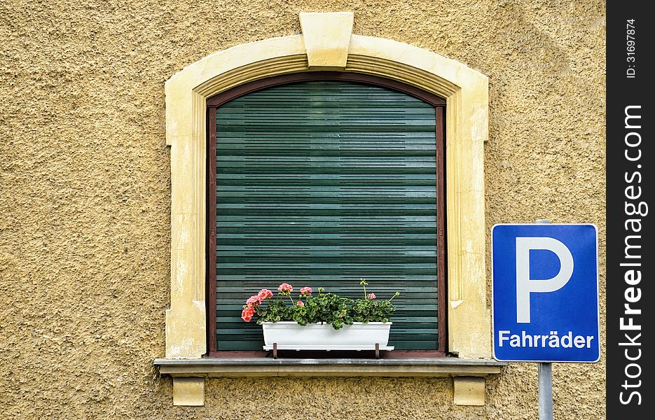 An European window with flowers and a bike parking board.