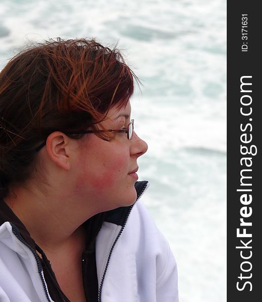 Teenage girl sat in front of a winter sea in the cold blowing wind looking out. Teenage girl sat in front of a winter sea in the cold blowing wind looking out.