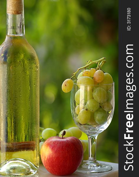 Bottle of white wine and fruit with full glass of grapes.