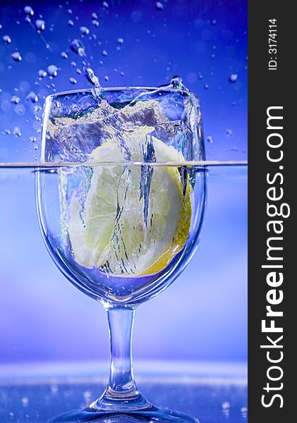 Lemon splash in transparent glass over blue background. Lemon splash in transparent glass over blue background