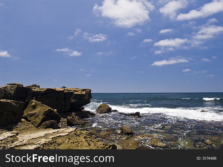 Ocean surf at low tide against a rock shoreline with deep blue sky