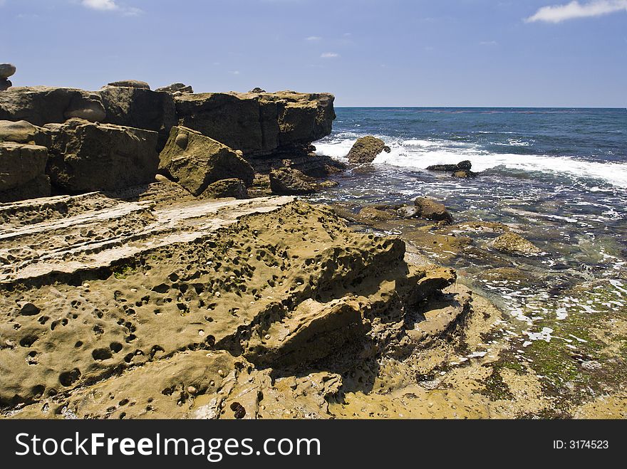 Ocean surf at low tide against a rock shoreline with deep blue sky