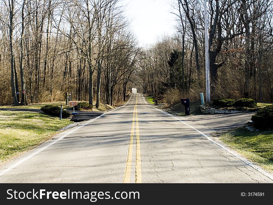 Double yellow line divides lanes on a country road in winter with barren trees