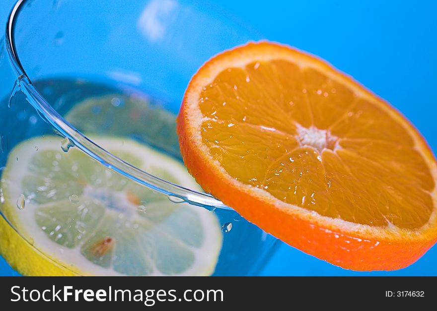 Oranges and lemons in transparent glass over blue background