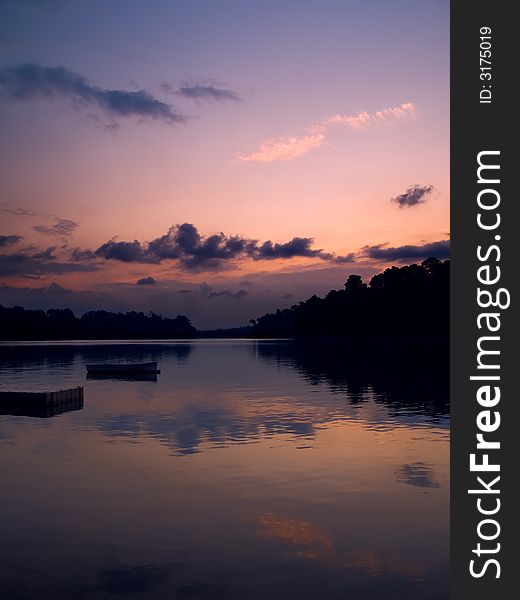 Boat moored off a pier in a reservoir used for kayak and canoe competition and training as seen just after the sun have descended below the horizon. Boat moored off a pier in a reservoir used for kayak and canoe competition and training as seen just after the sun have descended below the horizon.