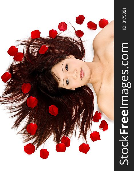 A young Asian woman lying on the studio floor with red rose petals. A young Asian woman lying on the studio floor with red rose petals