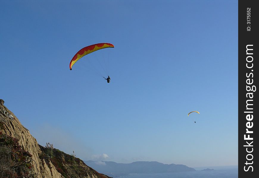 Two daring gliders having a great time catching thermals. At a cliff south of San Francisco on nice summer afternoon. Blue ocean and mountains in the background.