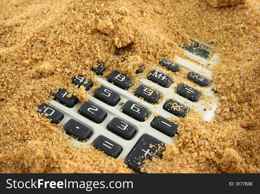 A calculator buried in the sand - buttons showing. A calculator buried in the sand - buttons showing