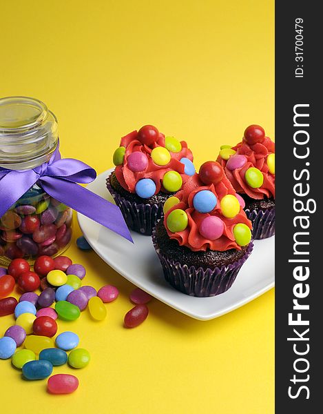 Bright colored candy cupcakes with candy jar - vertical.