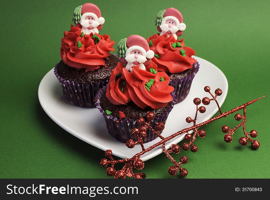 Three Christmas Cupcakes in purple polka dot wrapper with red frosting and santa decoration against a festive green background. Three Christmas Cupcakes in purple polka dot wrapper with red frosting and santa decoration against a festive green background