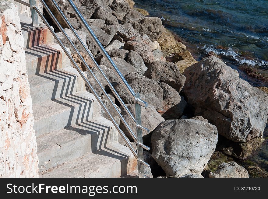 Stairs by the Mediterranean sea with rocks and zigzag shadow pattern. Mallorca, Balearic islands, Spain.