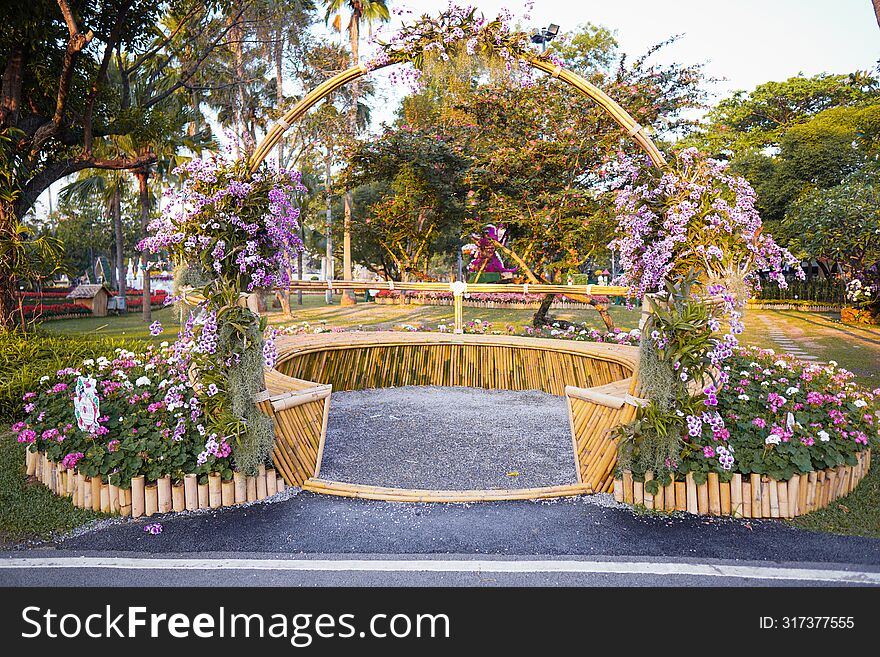 This Enchanting Garden Scene Showcases a Captivating Floral Archway, Inviting Viewers into a Lush Oasis. Adorned with Vibrant Purple Blooms and Nestled Amidst a Tranquil Park Setting, This Installation Blends Rustic Charm with Natural Beauty. the Bamboo Framing Adds an Eco-Friendly Touch, Enhancing the Organic Appeal of the Display.
