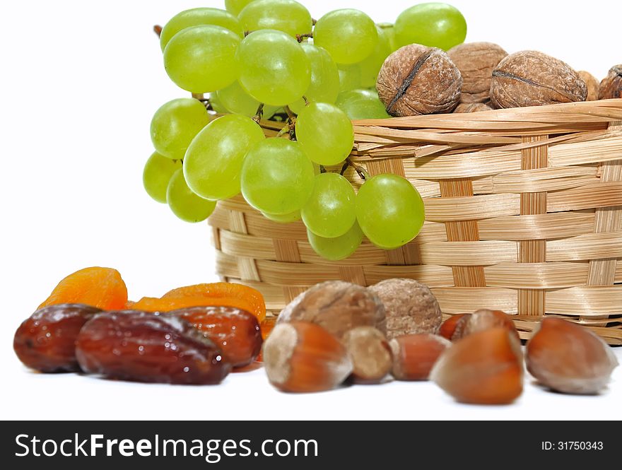 Dried fruits and grapes in a basket on white background