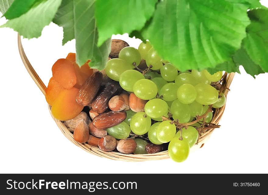 Dried fruits an grapes in a basket under foliage on white background. Dried fruits an grapes in a basket under foliage on white background