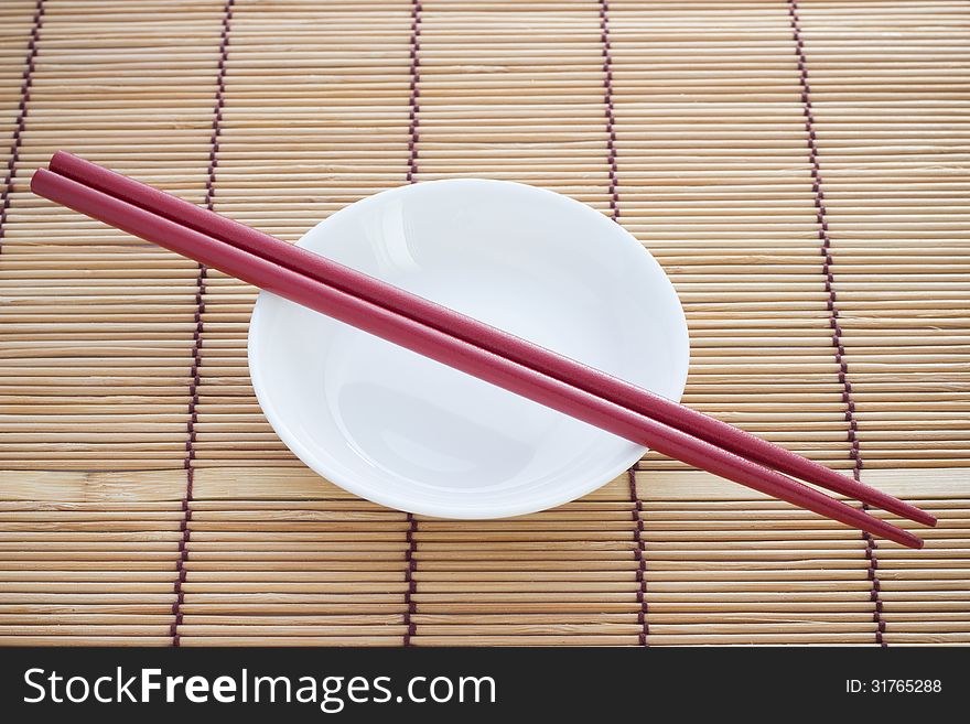 Two chopsticks next to a red and white bowl. Two chopsticks next to a red and white bowl