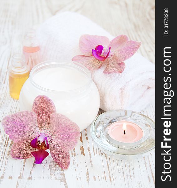 Container of cosmetic moisturizing cream with pink orchids and towel
