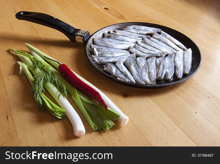 The process of cooking fish. Fresh fish on an old frying pan. Near vegetables (onions and peppers) on a wooden table.