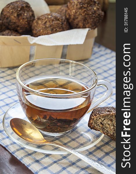 Glass cup of tea with golden spoon on an old table. Near basket with fresh bread. Glass cup of tea with golden spoon on an old table. Near basket with fresh bread