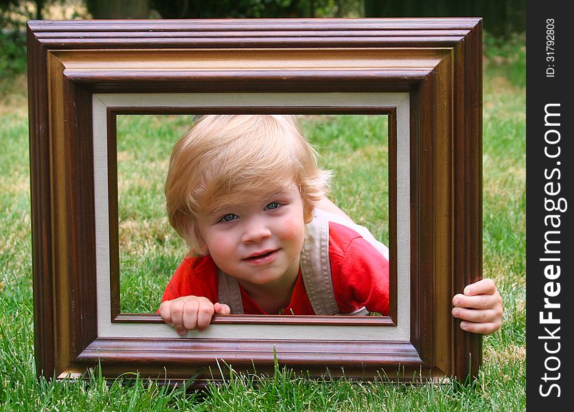 Cute little toddler boy laying on a lawn looking through a wooden frame. Cute little toddler boy laying on a lawn looking through a wooden frame.