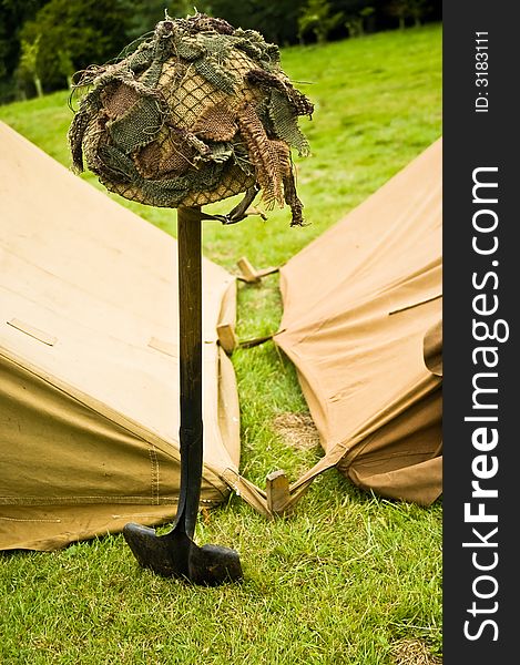 A WW II hard hat placed on a shovel in front of tents. A WW II hard hat placed on a shovel in front of tents.