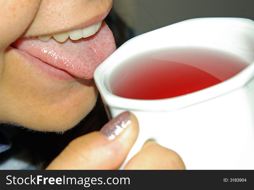 A girl tasting a red fruit tea from a white tea cup. A girl tasting a red fruit tea from a white tea cup