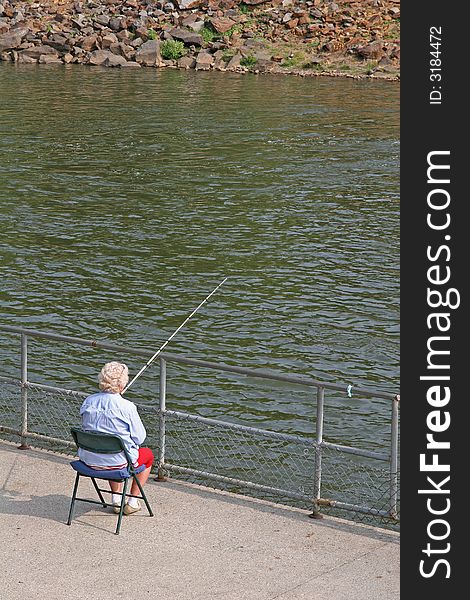 An old women sitting in a chair by the river fishing. An old women sitting in a chair by the river fishing